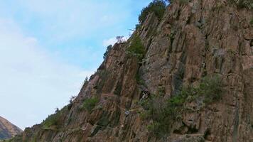 Drone footage captures a dramatic rocky sandstone cliff in a Kyrgyzstan mountain valley, revealing its texture and depth through a smooth tilt down when boom up camera movement with parallax effect, showcasing the remote, untouched landscape. video