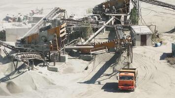 Aerial view of a sand or gravel crushing site with conveyor belts, machinery, and an orange truck. Dusty environment with piles of material, captured from above. video