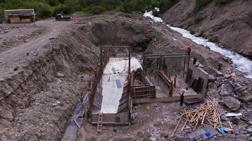 Aerial drone footage capturing builders constructing a reinforced concrete hydroelectric structure on the Tuyuk River in Belogorka, Kyrgyzstan - August 27, 2024 video