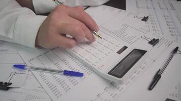 A focused person using a calculator surrounded by financial documents and pens for accurate calculations video