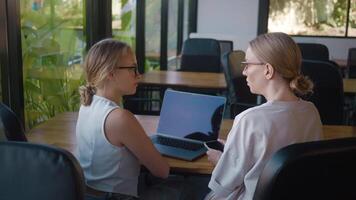 Two young ux designers collaborating in modern office, using laptop and smartphone to discuss ideas and strategies. Ux designers brainstorm interface solutions together, focusing on visual design. video