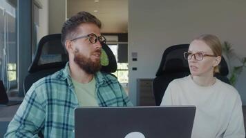dois colegas, homem e mulher, sentado às escrivaninha dentro moderno escritório, acionado dentro discussão sobre trabalhos projeto enquanto usando computador portátil. conceito do colegas discutir e resolver problemas às trabalhos dentro escritório video