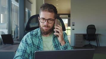 Young businessman working remotely from home office, using laptop and smartphone, managing finances, planning budget, and multitasking efficiently. Work Remotely from Home businessman video