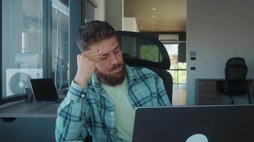 Office worker experiencing strong headache, feeling stressed and tired while working on laptop in office, dealing with work related pressure and exhaustion. Burnout and fatigue in office video
