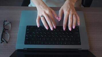 Woman office worker typing quickly on a laptop keyboard, focused on completing a project at her desk. Glasses resting nearby, showcasing a modern workspace filled with productivity video