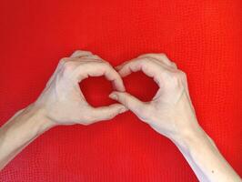 Hands forming a heart shape on a bright red background in a creative display of love or affection photo