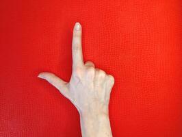 Hand gesture forming letter L against a vivid red background showcasing creativity and expression in art photo