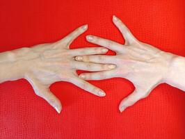Hands with elongated fingers positioned on a vibrant red background showcasing unique formations in a creative display photo