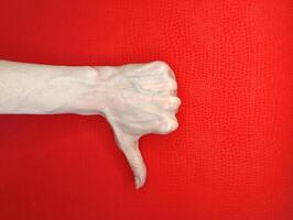 Hand gesture expressing disapproval against a vibrant red background with visible texture, symbolizing negativity and rejection photo