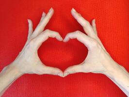 Hands forming a heart shape against a vibrant red background expressing love and connection photo
