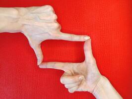 Hands framing a rectangular shape on a vibrant red background, highlighting a creative gesture in a playful atmosphere photo