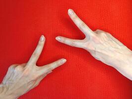 Hands forming peace signs against a vibrant red background displaying creativity and expression photo