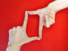Creative hand gestures frame a square shape against a vibrant red background in a playful and artistic display photo