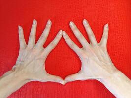 Hands forming a heart shape on a vibrant red textured background in natural light photo