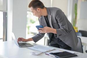 a businessman in a suit holding a cell phone and looking at his laptop photo