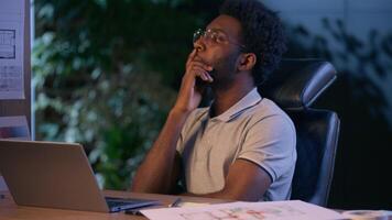 Thoughtful businessman African American business man designer thinking design project consider architecture plan online late working in dark night office typing laptop architect think creative ideas video
