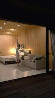 Young woman wearing a bathrobe stretches and dances in a modern and minimalist bedroom with wooden walls, enjoying a relaxing evening at home video