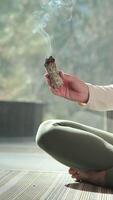 Wellness practitioner performing sage smudging ritual, waving burning white sage bundle while meditating, cleansing negative energy and promoting inner peace and tranquility video