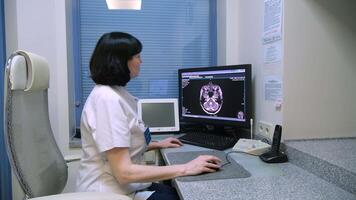 Female doctor carefully examines a brain scan displayed on a computer monitor, utilizing specialized medical software in a modern hospital or clinic setting video