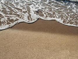 Ocean foam gently touching smooth brown sand surface in minimalist seashore abstract texture background Gentle ocean wave meeting smooth sand in calming symmetrical beach background ideal for wellness photo