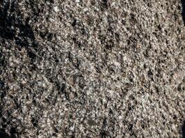 Macro view of urban asphalt filled with quartz and stone particles capturing raw textured pattern of pavement surface under natural sunlight photo