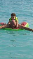 Vertical . Father and son having fun during summer vacation. Dad and child swim on inflatable ring in sea video