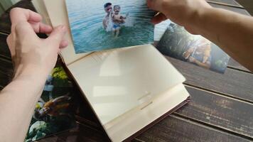 Father day. Printed photographs capturing joyful family memories in summer. Hand places picture into photo album. Image features son sharing a laugh with his father. video