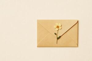 Kraft envelope with dried yellow flower on beige background, minimal composition for greeting or wedding stationery photo