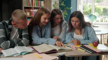Four teenagers group classmates reading book together preparing for exams doing homework talking discuss read education studying learning pupils in school library teamwork knowledge teens educate task video