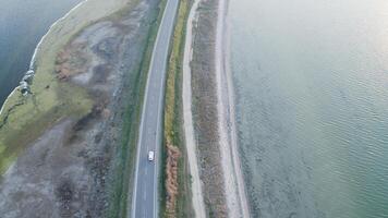 top down view of a lone white car driving on a rural highway surrounded by lakes. photo