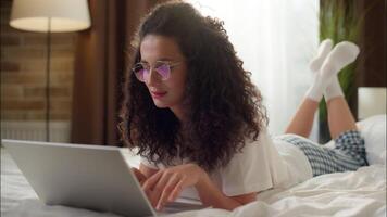 Woman relaxing in bed with laptop Caucasian girl browsing web search internet store using computer in bedroom attractive female shopping online at home ordering goods buying comfort distant education video