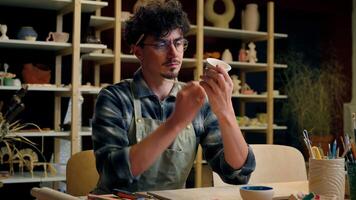 Man artist potter designer craftsman painting master class drawing aquarelle in creative pottery workshop art studio male guy painter decorator artisan paint artwork ornament craft ceramics handmade video