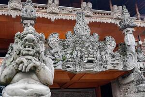 Close-up of a Balinese guardian statue and elaborately carved temple gate at a traditional building in Bali, Indonesia. photo