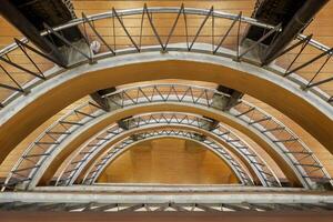 Abstract geometric architecture with circular metal beams and wood panels viewed from below, featuring symmetrical industrial design and modern interior elements. photo