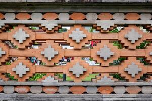 Traditional Balinese brick wall with decorative geometric patterns made from red and grey stone. A detail of cultural architecture found in temples and heritage sites in Bali, Indonesia. photo