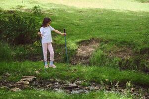 Young Girl Exploring Nature With Walking Sticks Near a Creek in a Scenic Park photo