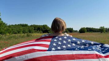 A young Caucasian boy stands in a field wrapped in an American flag, symbolizing patriotism and freedom Independence Day and nationalism are highlighted video