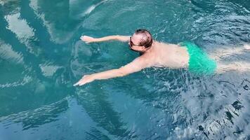 A Caucasian man swims in a pool wearing green trunks, celebrating relaxation and summer vacation video