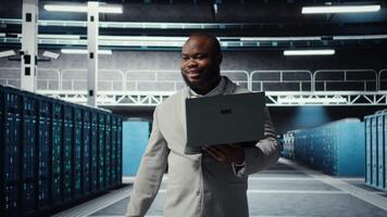 Server room worker auditing systems for vulnerabilities using software on laptop. Engineer walking in data center doing backups and recovery protocols using notebook, camera A video