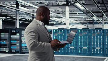 Server room infrastructure engineer scripting automated workflows using software on laptop. Data center programmer running predictive maintenance scans using notebook, camera A video