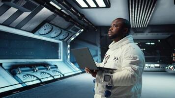 Astronaut in spacecraft using laptop to run telemetry data analysis. Man in spaceship wearing spacesuit analyzing mission logs on notebook during planetary exploration, camera A video