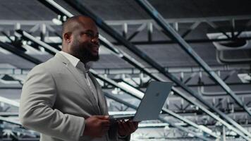 Admin walking in data center industrial platform analyzing infrastructure performance outputs on laptop. Server farm worker doing job tasks, finetuning mainframes configurations, camera B video