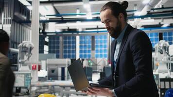 Facility supervisor in a suit monitoring solar panel assembly line, reflecting professional occupation and executive level involvement in renewable energy growth. Sustainability. Camera B. video