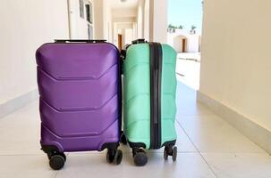 Two colorful suitcases stand side by side in a sunny hotel corridor, ready for travel or vacation. Bright architecture and palm trees hint at a warm destination photo