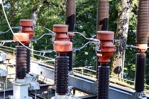 Close-up of a power transformer with cooling fins, high-voltage insulators, and overhead wires. Industrial electricity infrastructure under blue sky. photo