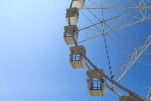 A close-up view of the cabins of a Ferris wheel against a vibrant blue sky on a sunny day. The white structure contrasts beautifully with the clear sky, creating a cheerful summer atmosphere photo