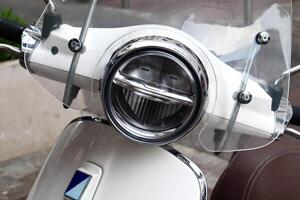 Close-up of a modern white scooter headlight with a transparent windshield. The chrome details shine brightly, highlighting the sleek urban design. photo