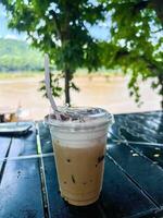 A cup of iced coffee sitting on a table in front of a river photo