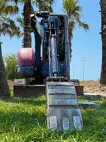 Excavator Bucket Resting on Grass with Palm Trees in Background photo