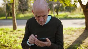 Bald Elderly Man Sitting in the Park Using His Smartphone video